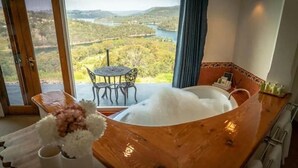 A room with a large bathtub, a table with chairs, and a view of a lake and forest. - Eagle View Escape (Rydal)