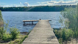 Une jetée en bois s’étendant sur un lac paisible, avec une rive boisée en arrière-plan.