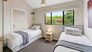 Une chambre avec deux lits, une fenêtre donnant sur un espace verdoyant, une table de chevet avec une lampe et une porte.