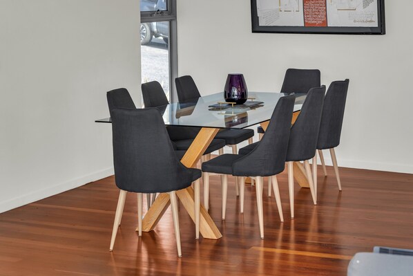 A modern dining area with a glass table surrounded by six chairs with wooden legs.