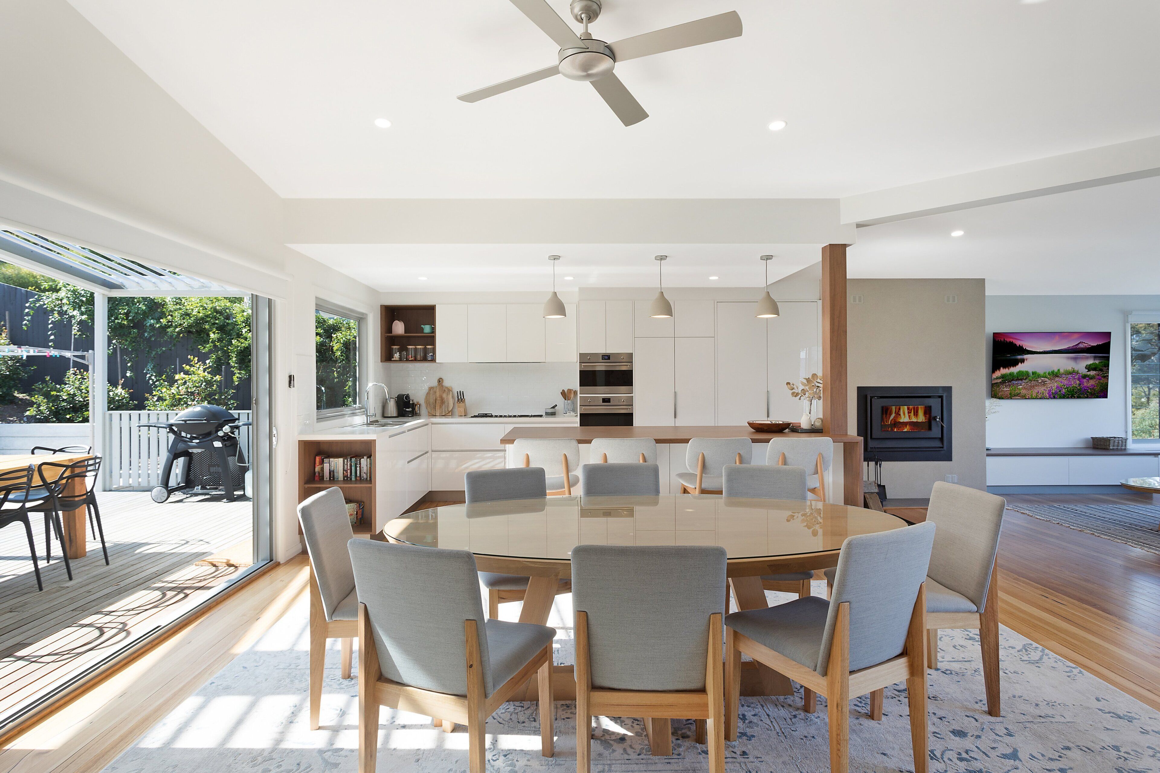 A modern dining area with a round table, multiple chairs, and a ceiling fan.