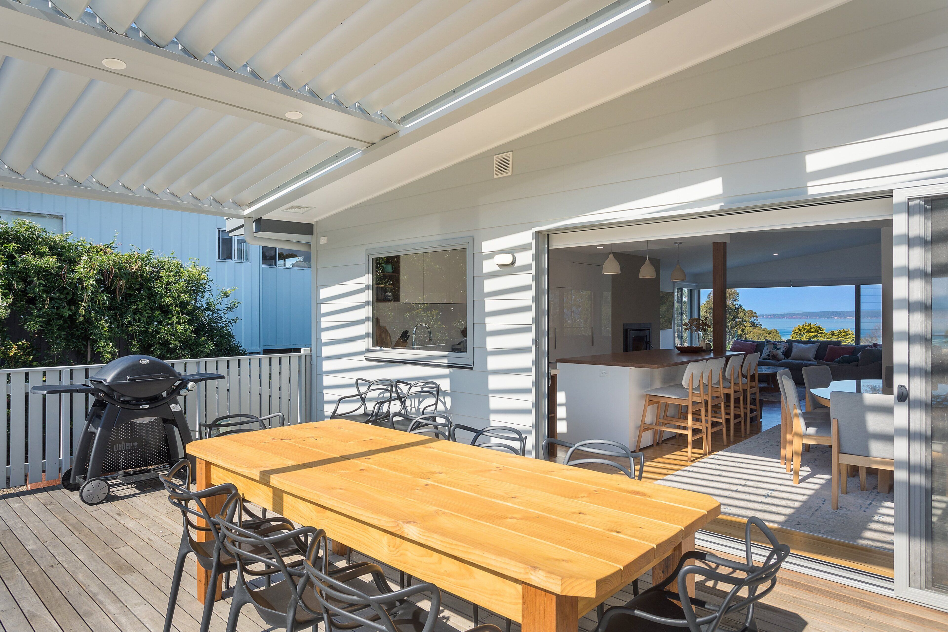 Une terrasse extérieure avec une table et des chaises en bois, un barbecue et une vue sur la mer.