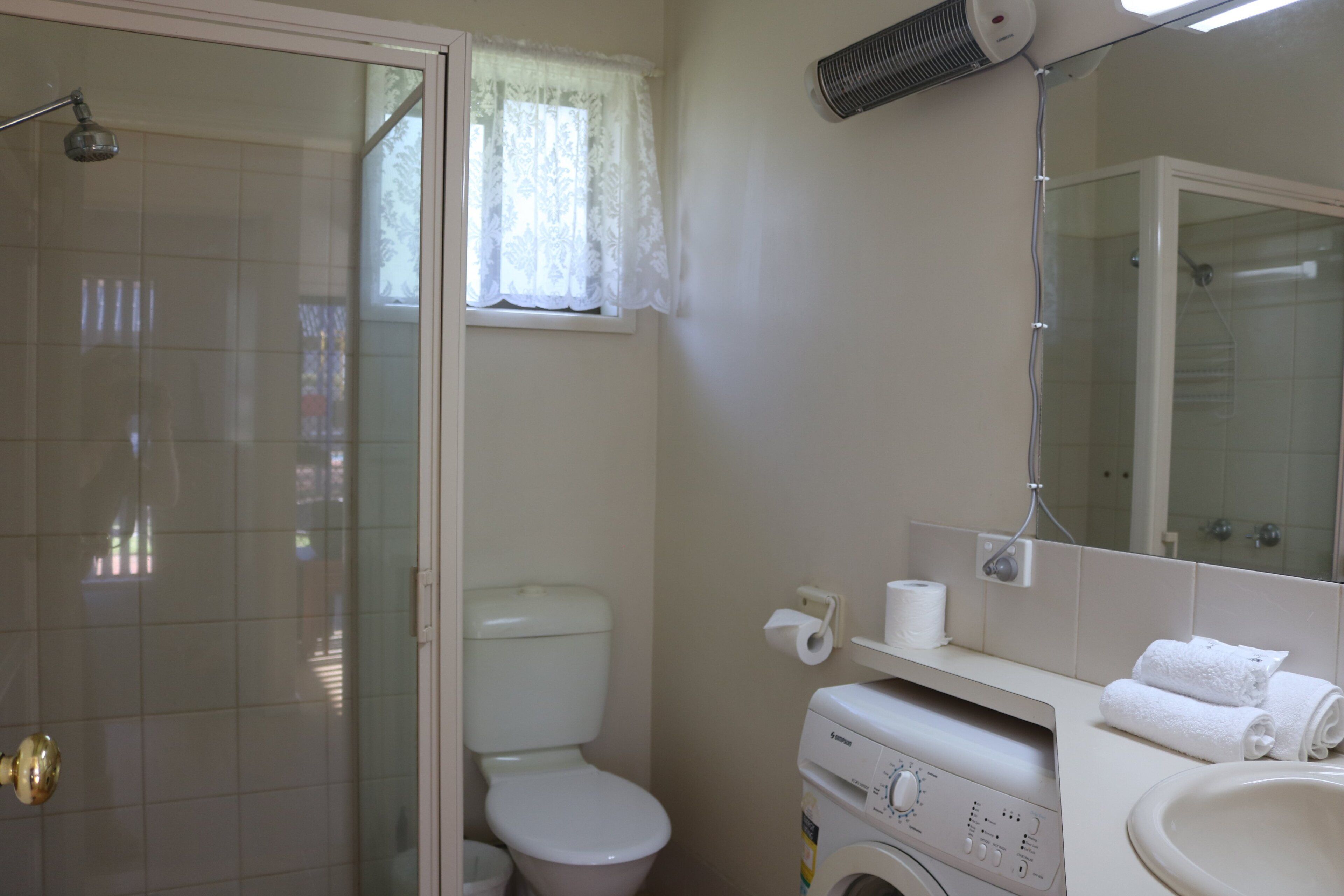 A bathroom with a glass-enclosed shower, a toilet, a washing machine, and a sink.