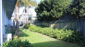 A backyard with a wooden fence, a lawn, and various plants. - Admirals Lodge: Unit 1: Pet friendly (Merimbula)