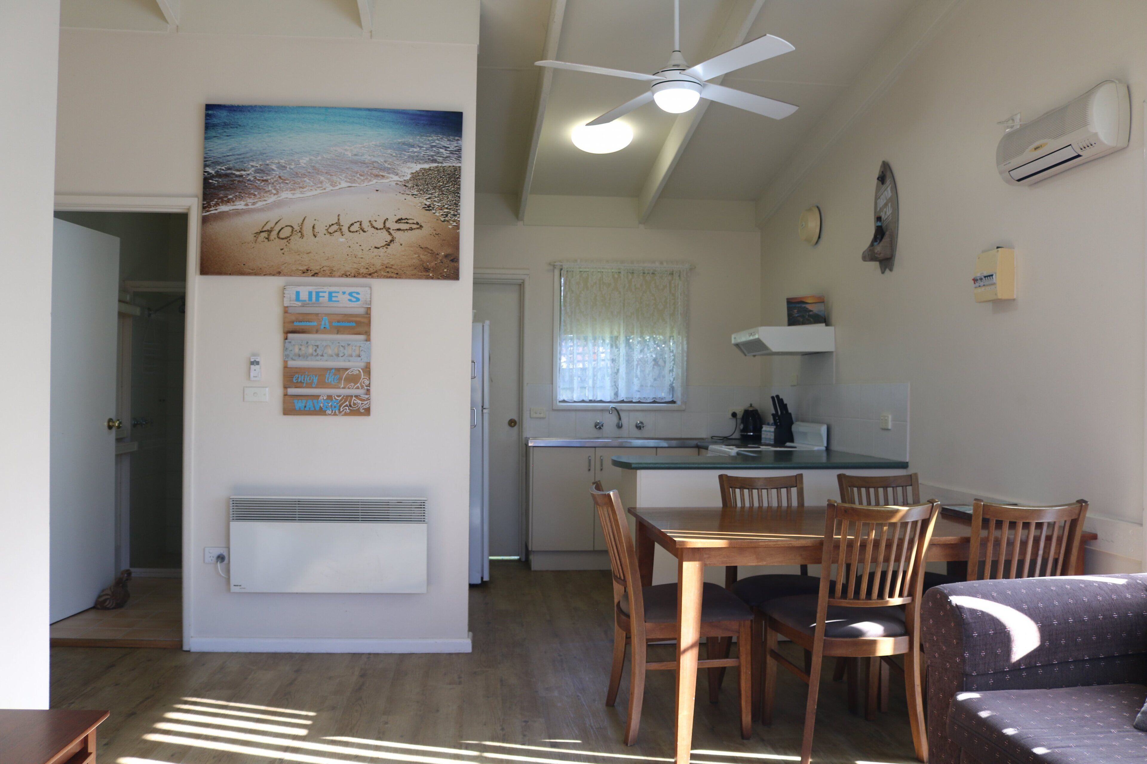 Eine kompakte Küche mit Essbereich, Deckenventilator und einer Wanddekoration im Strandstil.