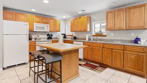A kitchen with wooden cabinets, a white refrigerator, a microwave, a stove, and a bar area with stools. - E. Rochester Darling - Sleeps 6! (East Rochester)