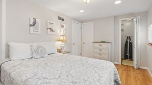 A bedroom with a large bed, a bedside table with a lamp, a dresser, and a door leading to a bathroom. - E. Rochester Darling - Sleeps 6! (East Rochester)