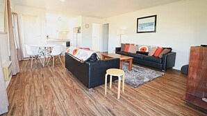 A modern living room with a black sofa, white chairs, a wooden coffee table, and a grey rug. - Beachcomber: Unit 3 (Upstairs) (Merimbula)