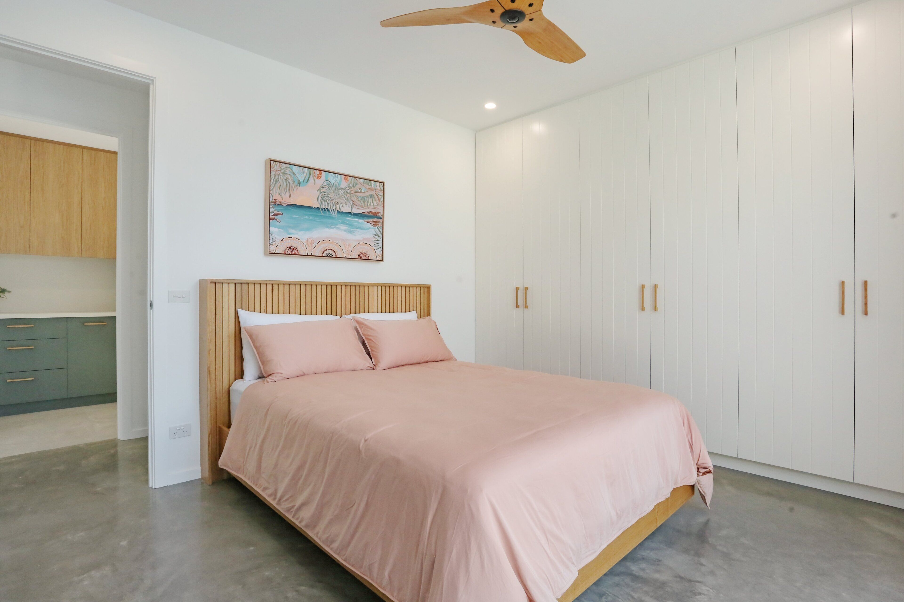Une chambre à coucher avec un lit, un ventilateur de plafond, un tableau et une armoire.