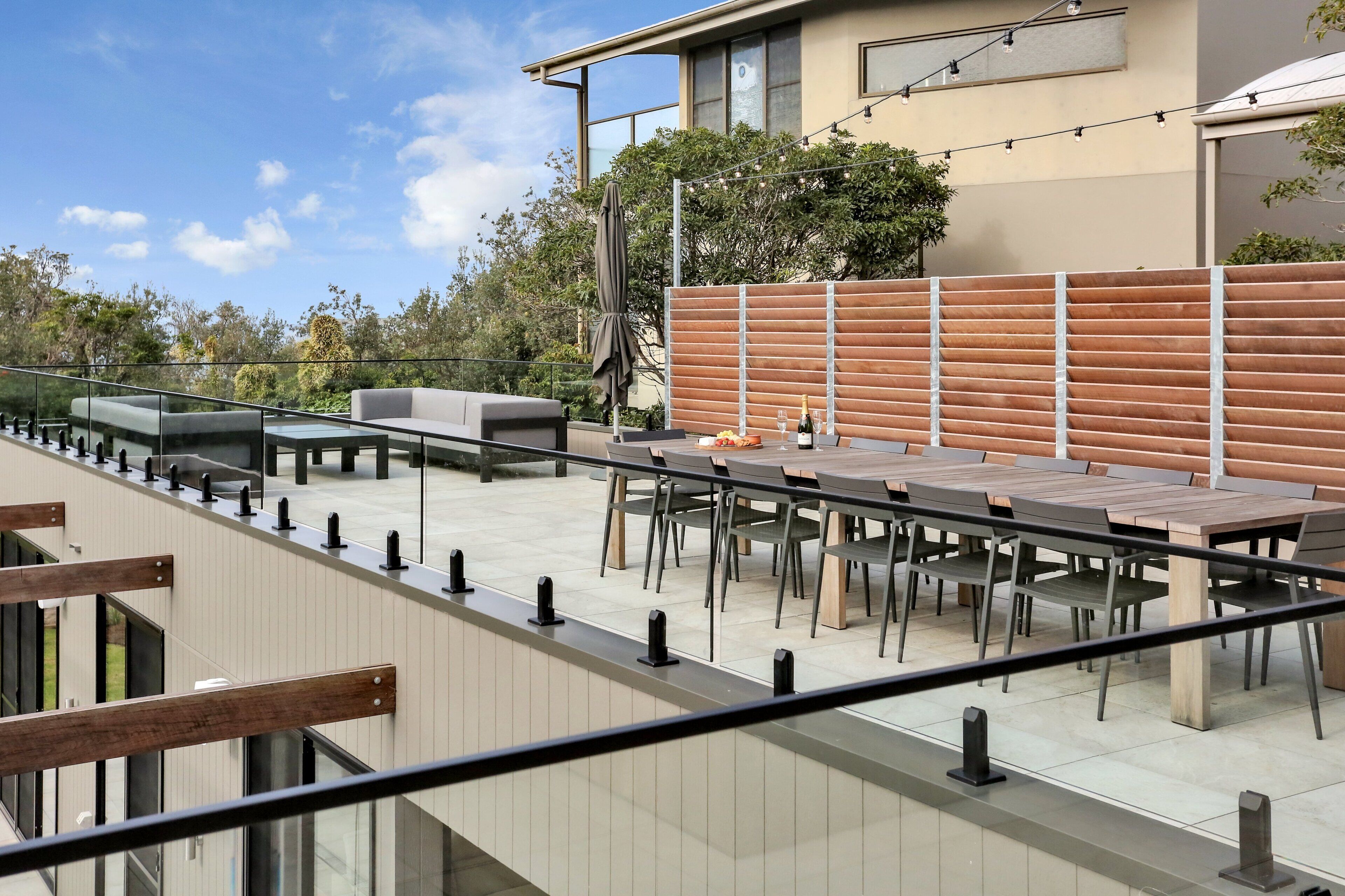 An outdoor patio with multiple tables and chairs, a wooden fence, and a modern building in the background.
