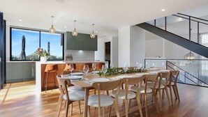 Een moderne keuken met een groot eiland, een houten eettafel en stoelen. Er is een trap met een glazen balustrade die naar een hoger niveau leidt.