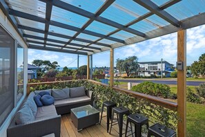 A covered outdoor area with a sofa, a small table, and two stools.
