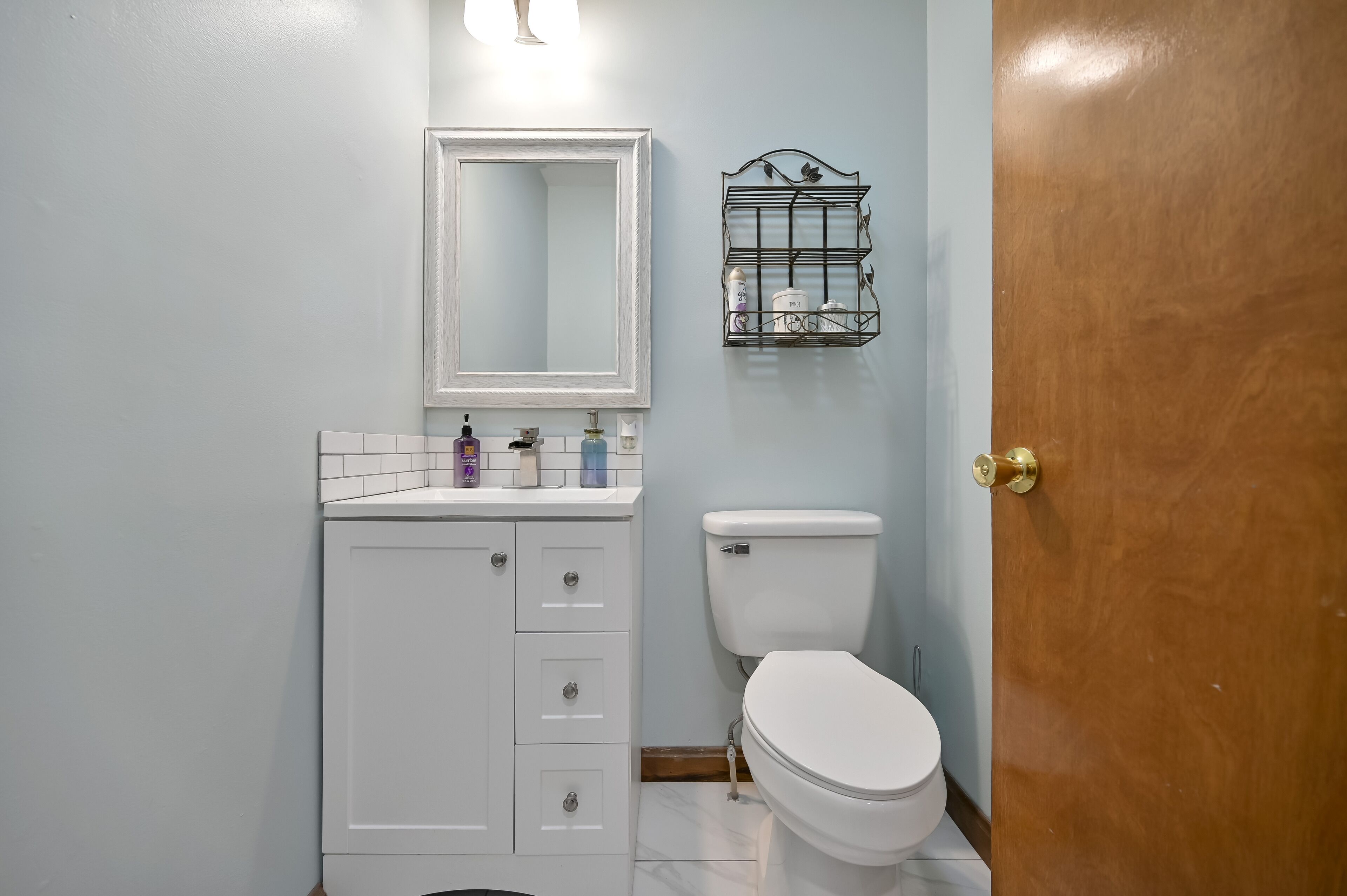 A bathroom with a white toilet, a white sink with a mirror above it, and a wooden door.