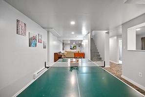 Um quarto amplo com mesa de pingue-pongue, escada e um espaço de estar acolhedor com sofá e mesa lateral.