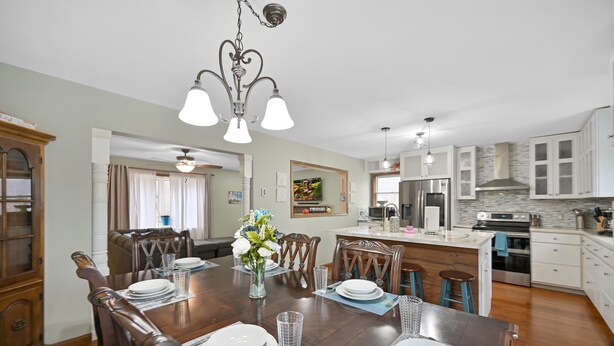 A dining area with a wooden table set for four, surrounded by chairs. There is a chandelier above the table, and a kitchen area is visible in the background. - Poconos Peaceful Retreat. Short drive to Ski, Swim, Hike, or Shop! 4 Bedrooms. (Tobyhanna)