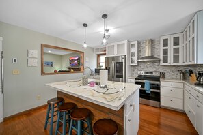 Uma cozinha moderna com armários brancos, uma ilha grande com banquetas, eletrodomésticos de aço inoxidável e um revestimento de azulejos.