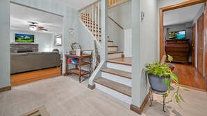 A modern living room with a grey sofa, a wooden staircase, and a potted plant. - Poconos Peaceful Retreat. Short drive to Ski, Swim, Hike, or Shop! 4 Bedrooms. (Tobyhanna)