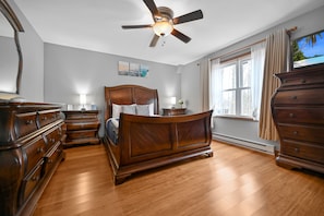 Um quarto espaçoso com uma cama grande, móveis de madeira, um ventilador de teto e uma janela com cortinas.