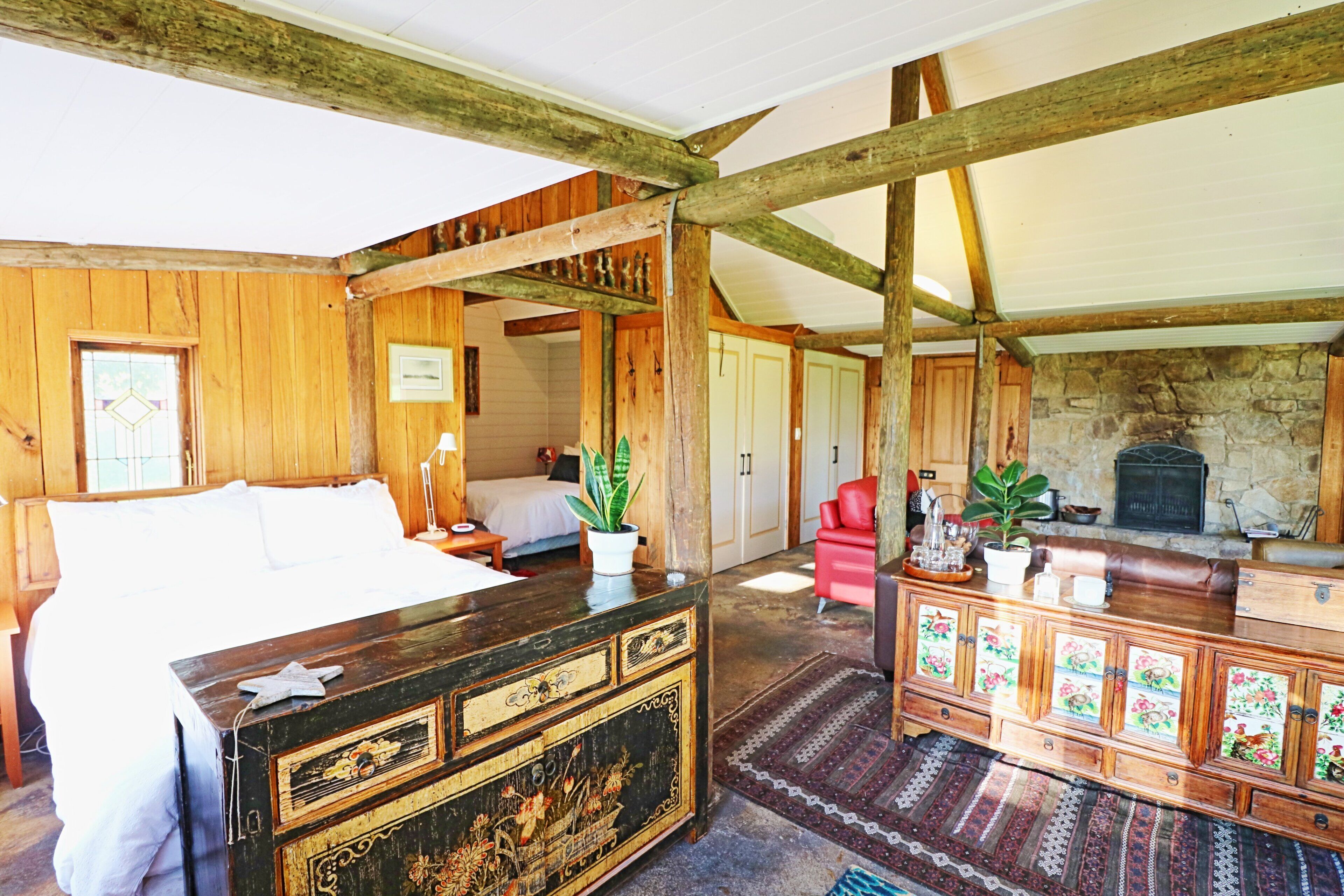 Una habitación rústica con cama, muebles de madera, chimenea de piedra y una silla roja.