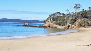Ein Strand mit klarem, blauem Wasser, Sandstrand und Felsen.