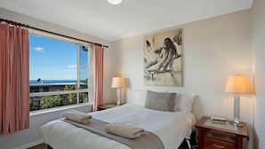 Ein Hotelzimmer mit einem großen Bett, zwei Nachttischen mit Lampen, einem Bild an der Wand und Blick auf die Stadt durch das Fenster.