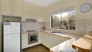 Una cucina compatta con pensili bianchi, forno a incasso, frigorifero e una finestra vista verde.