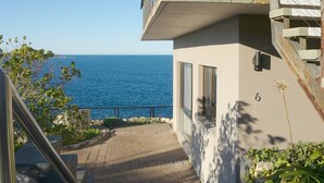 Un edificio moderno con un balcone vista mare, un vialetto lastricato e il numero '6' sulla parete.