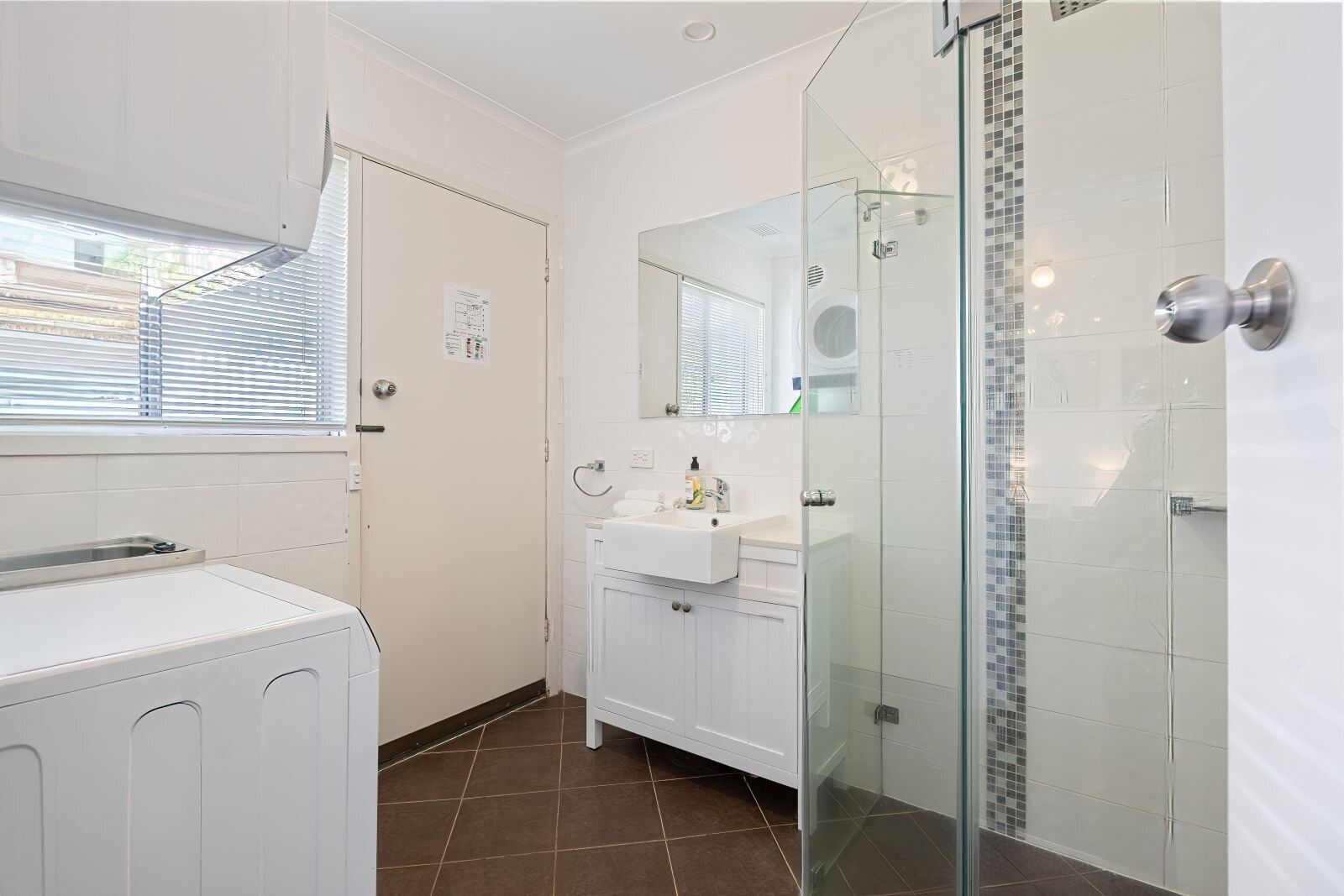 A modern bathroom with a glass-enclosed shower, a white sink, and a laundry area.