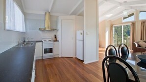 Cozinha moderna com eletrodomésticos brancos, área de refeições com mesa de vidro e vista para o exterior.