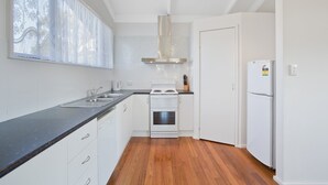 Een keuken met witte kasten, een zwart aanrecht, een fornuis, een koelkast en een raam met dunne gordijnen.