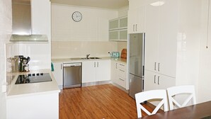 A modern kitchen with white cabinets, a stainless steel refrigerator, a dishwasher, and a built-in oven. - Jodi's Beach Retreat: 2 bedroom pet friendly apartment (Eden)