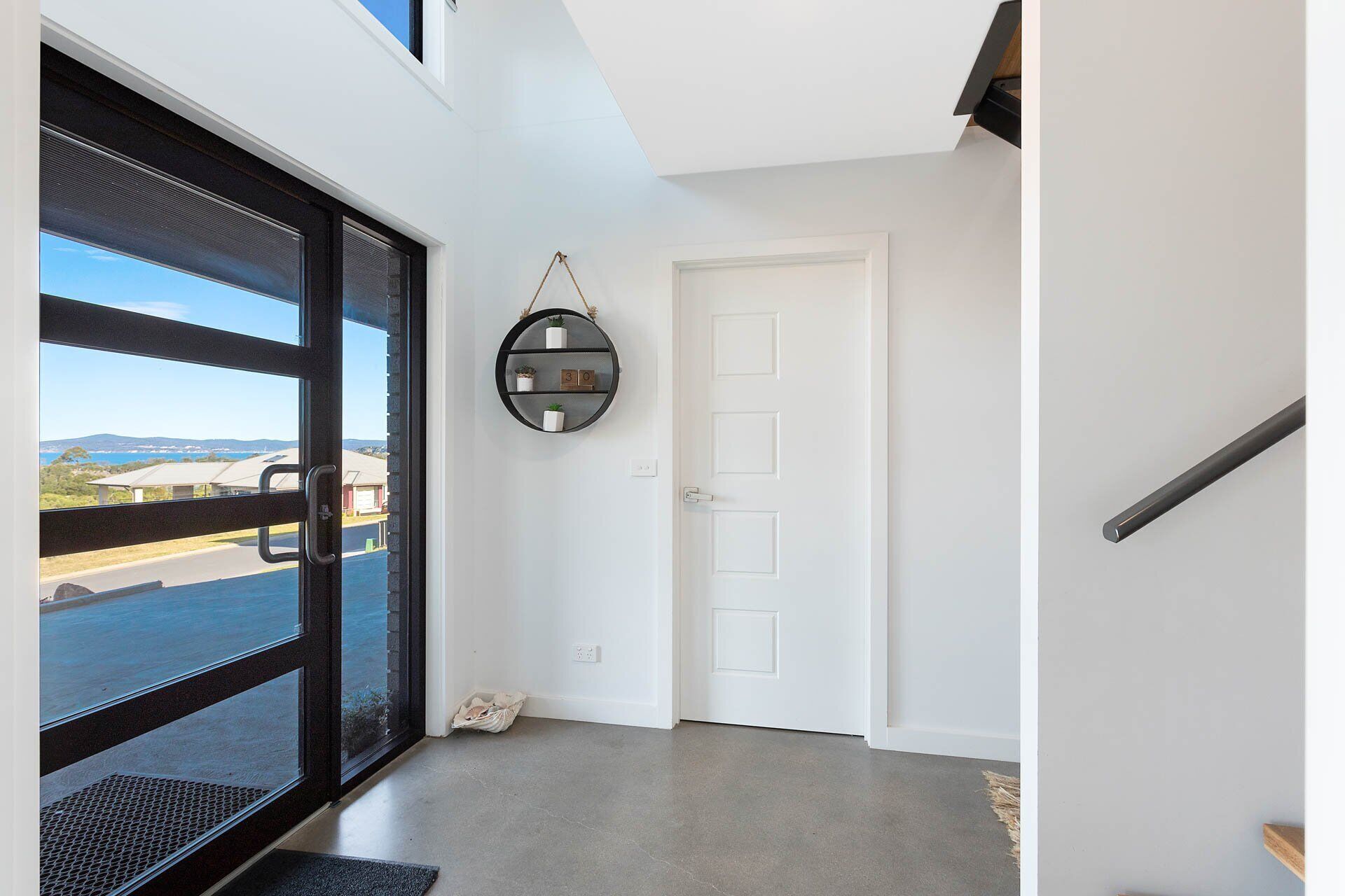 A modern interior with a large glass door leading to a balcony, a white door, and a round shelf with potted plants.