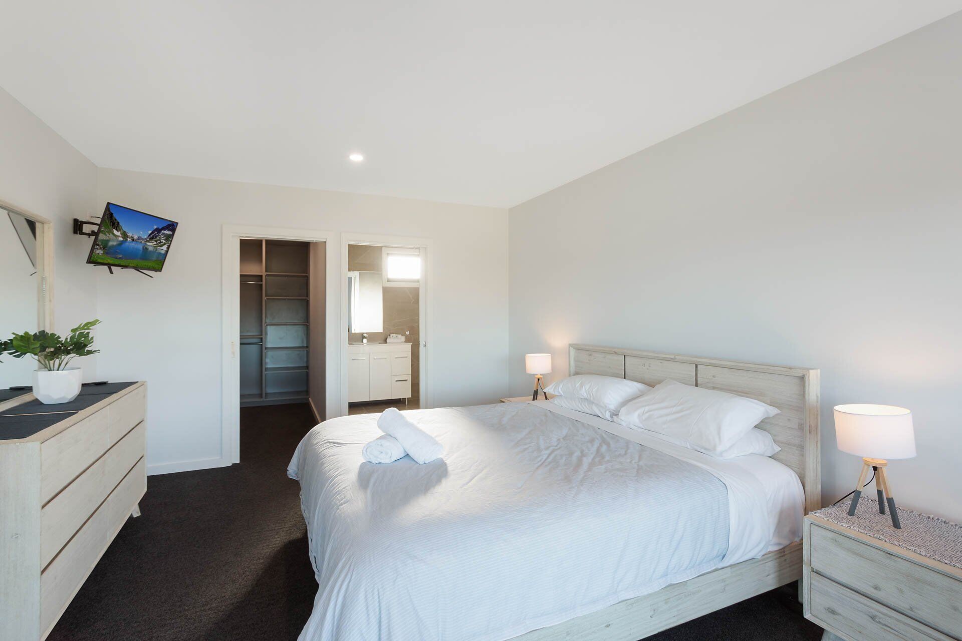 A hotel room with a bed, bedside tables, a dresser, a TV mounted on the wall, and a walk-in closet.