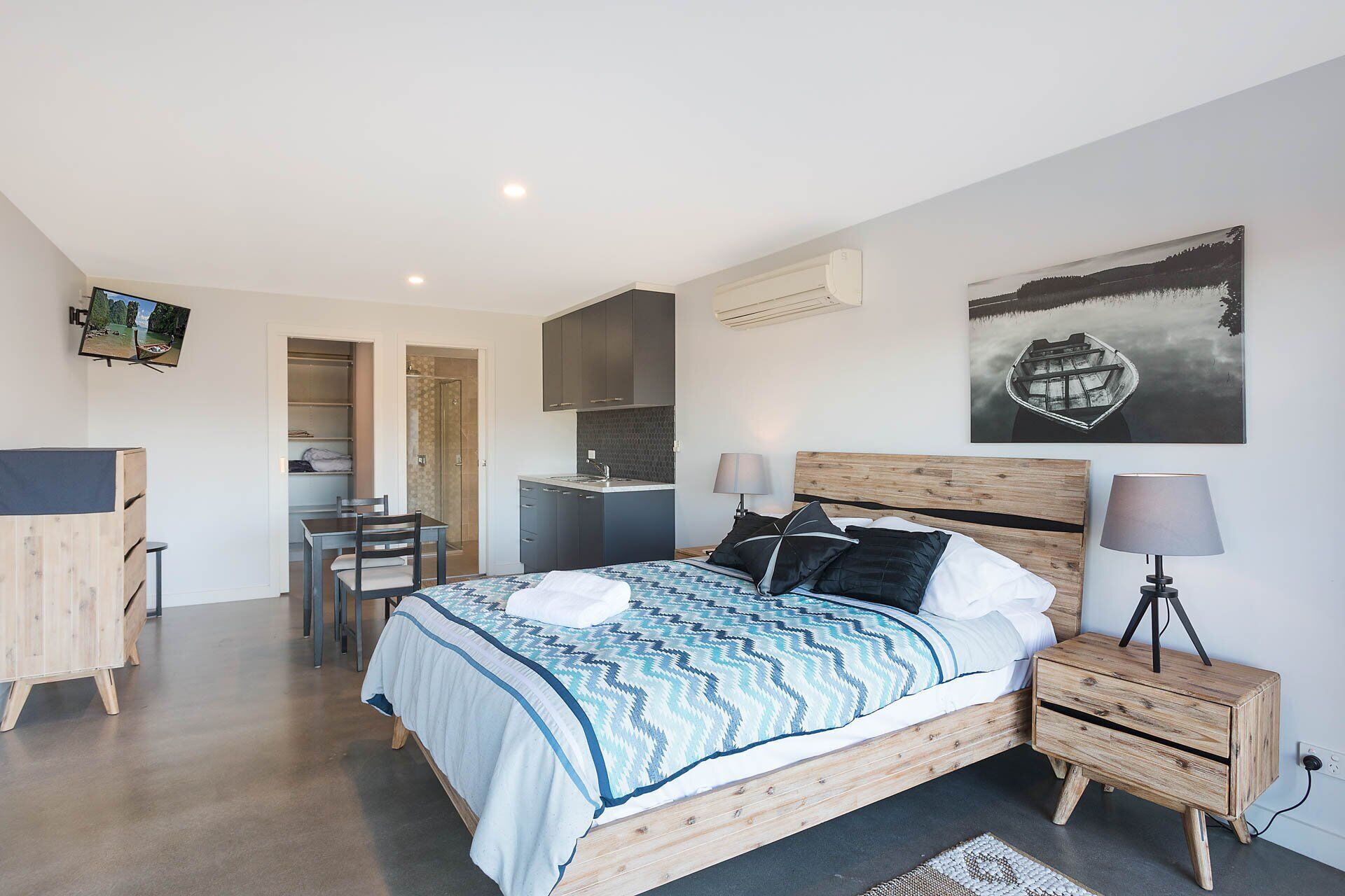 A modern bedroom with a bed, bedside tables, a desk, and a shower area.