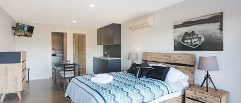 A modern bedroom with a bed, bedside tables, a desk, and a shower area.