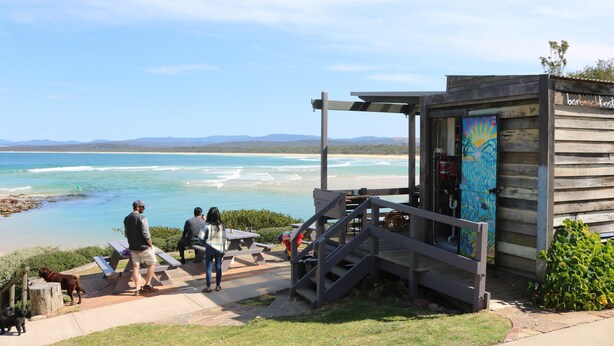 A wooden structure with a beach view, a covered seating area, and a staircase leading to a door.