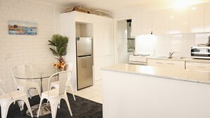 A modern kitchen with white cabinets, a stainless steel refrigerator, and a glass dining table with chairs.