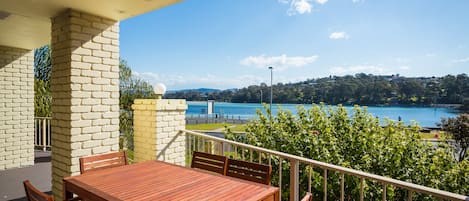 A wooden table and chairs on a balcony with a view of a lake and hills.