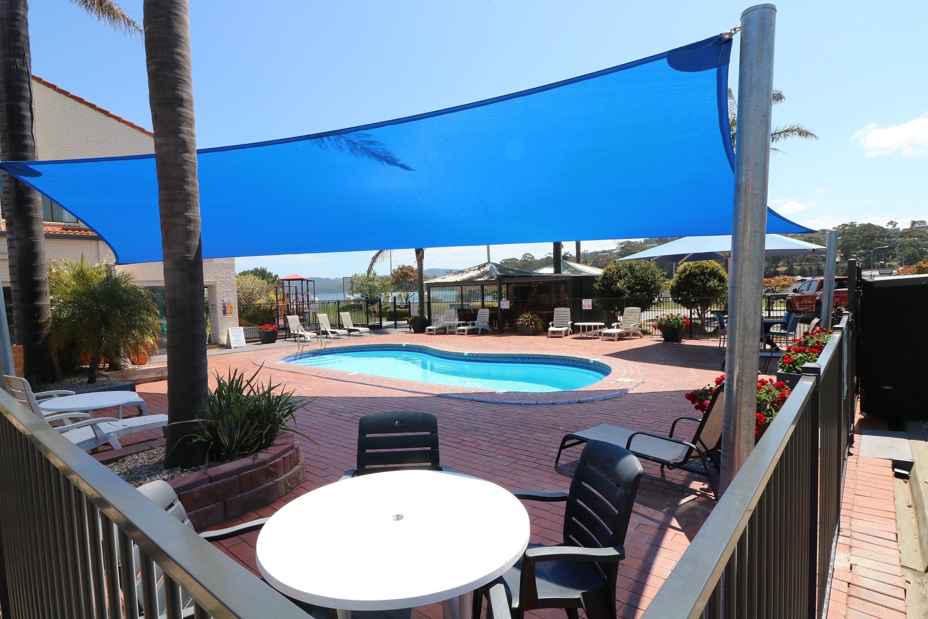 A pool area with lounge chairs and a table, shaded by a blue canopy.