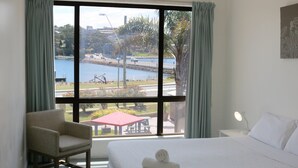 A hotel room with a large window, a bed, a chair, and a table with a lamp. - Aquarius Merimbula 3 bedroom Lake View (Merimbula)