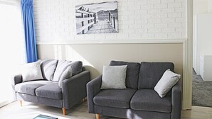 Two grey sofas with cushions, a white brick-patterned wall, and a black and white photograph of a pier. - Aquarius Merimbula 3 bedroom Lake View (Merimbula)