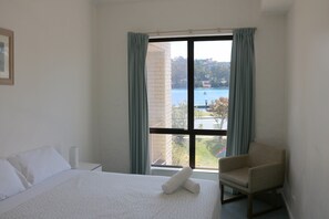 Une chambre d’hôtel avec un lit, une chaise et une grande fenêtre donnant sur un plan d’eau et des bâtiments.