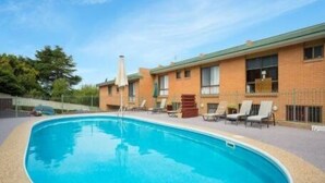 Una piscina con sillas de descanso y sombrillas, rodeada por un edificio de ladrillo con techo verde.