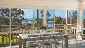 A covered outdoor dining area with a table and chairs, large windows offering a view of a lake and surrounding landscape. - Pelican Lake House - 4 bedroom pet friendly (Merimbula)