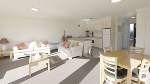 A modern living room with a sofa, coffee table, and dining table. - Pelican Waters Unit 1, ground level accommodation (Merimbula)