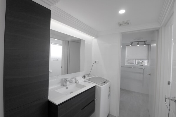 Un bagno moderno con un mobile lavabo in legno scuro, un ampio specchio e una lavatrice integrata.