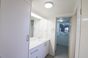 A compact bathroom with a white sink, mirror, and cabinets. - Pelican Waters Unit 2, ground level accommodation (Merimbula)