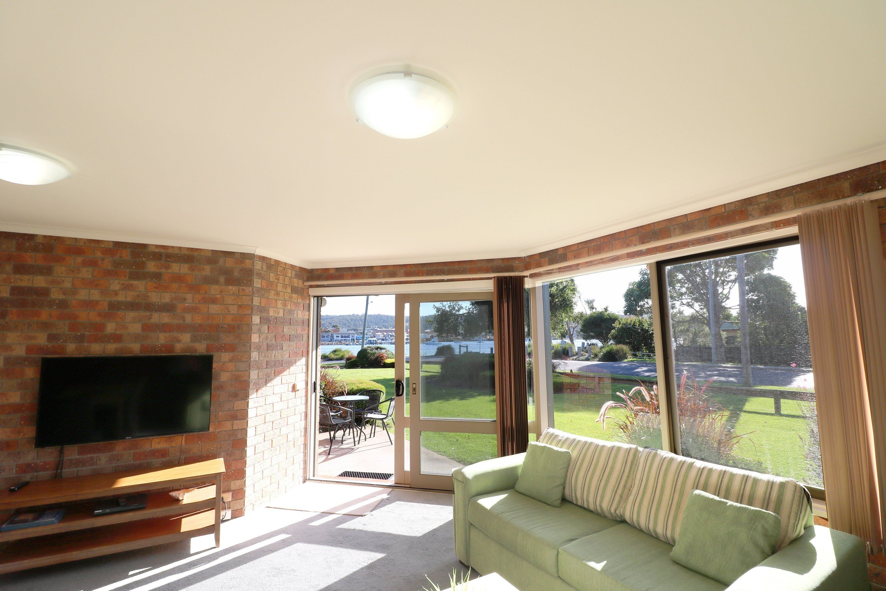 A living room with a TV on a brick wall, a sofa, and a sliding glass door leading to a patio.
