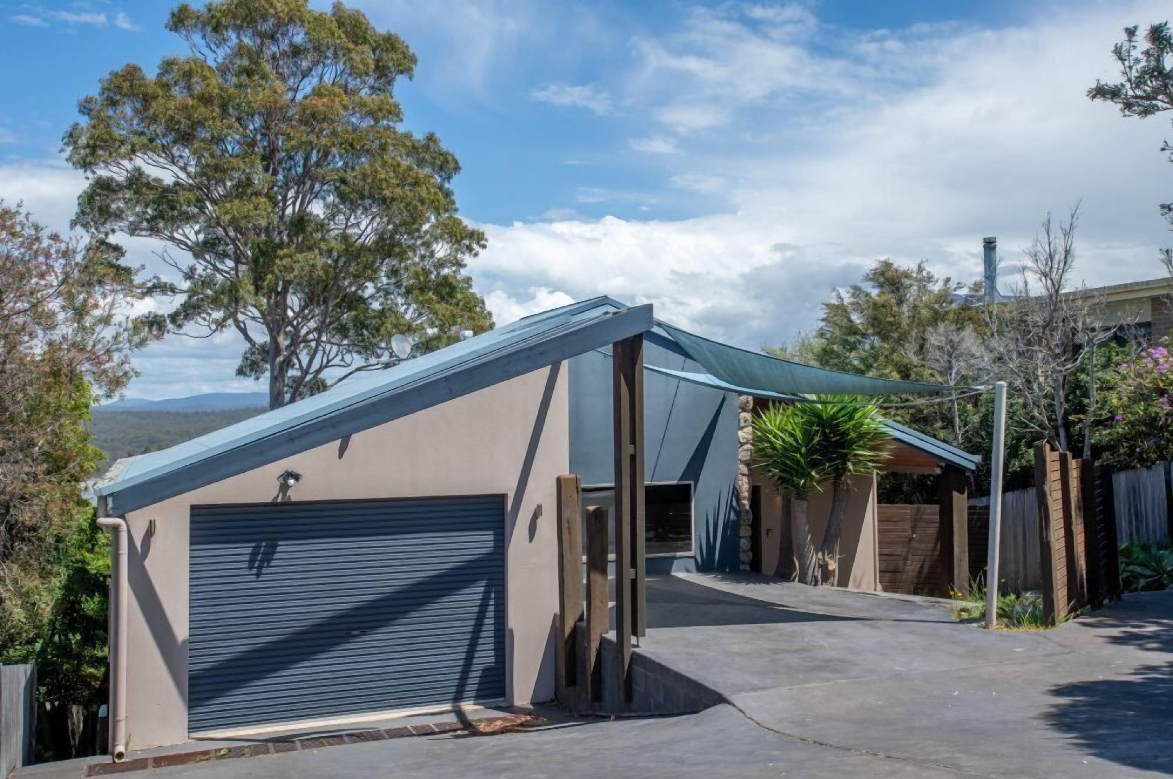 A modern garage with a sloped roof, a closed garage door, and a covered driveway area.