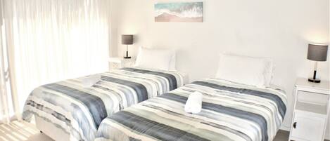 A hotel room with two beds, white bedding, a nightstand with a lamp, and a painting on the wall.